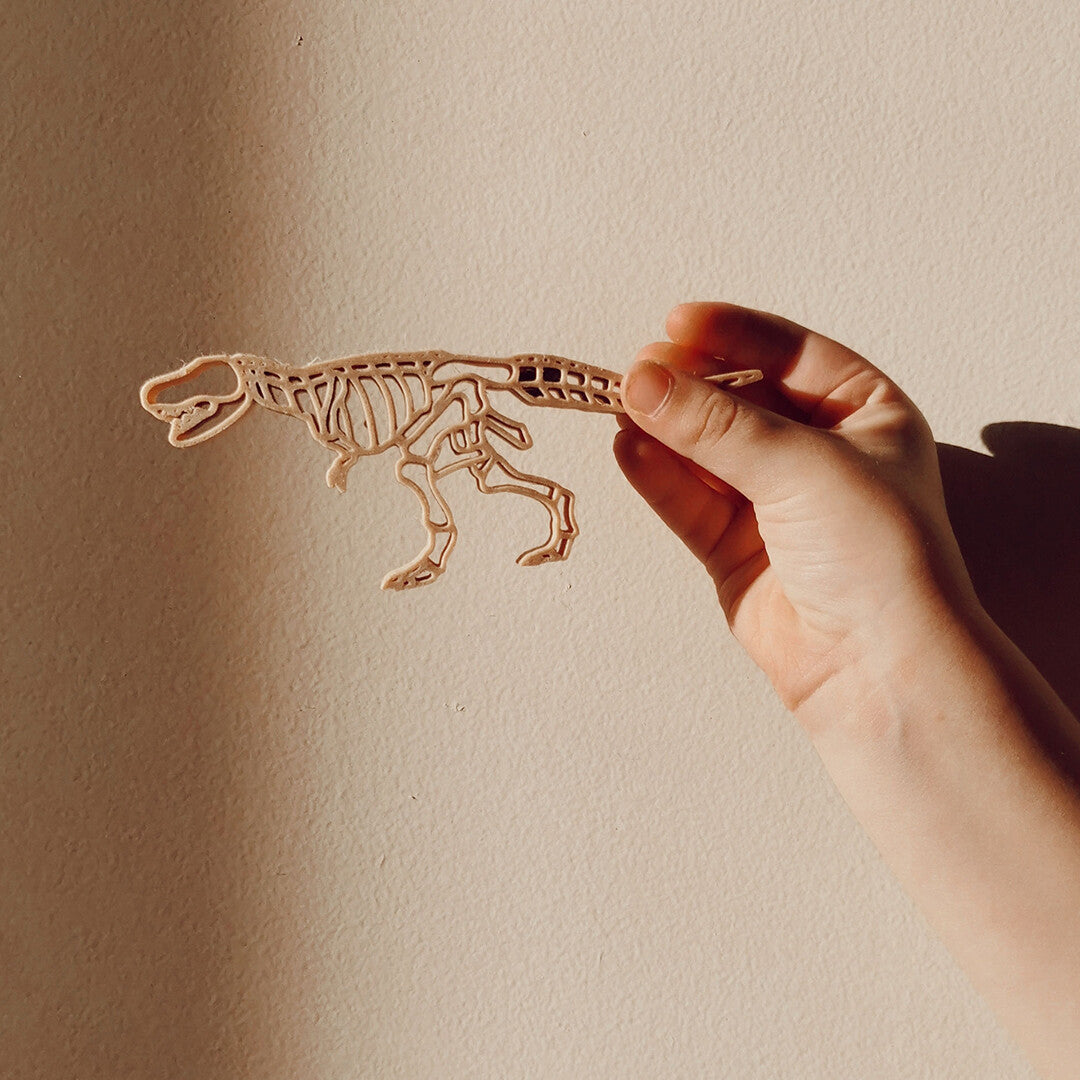 Een hand houdt de grennn houten uitsteekvorm van een dinoskelet vast.