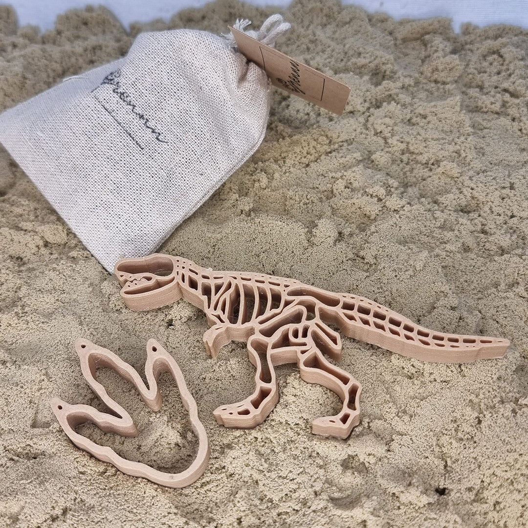 De grennn houten uitsteekvormen van een dinoskelet en pootafdruk liggen op zand naast een stoffen zakje.