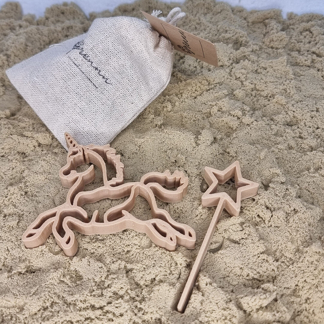 Grennn uitsteekvormen van een eenhoorn en een toverstaf in het zand, met een linnen zakje op de achtergrond.