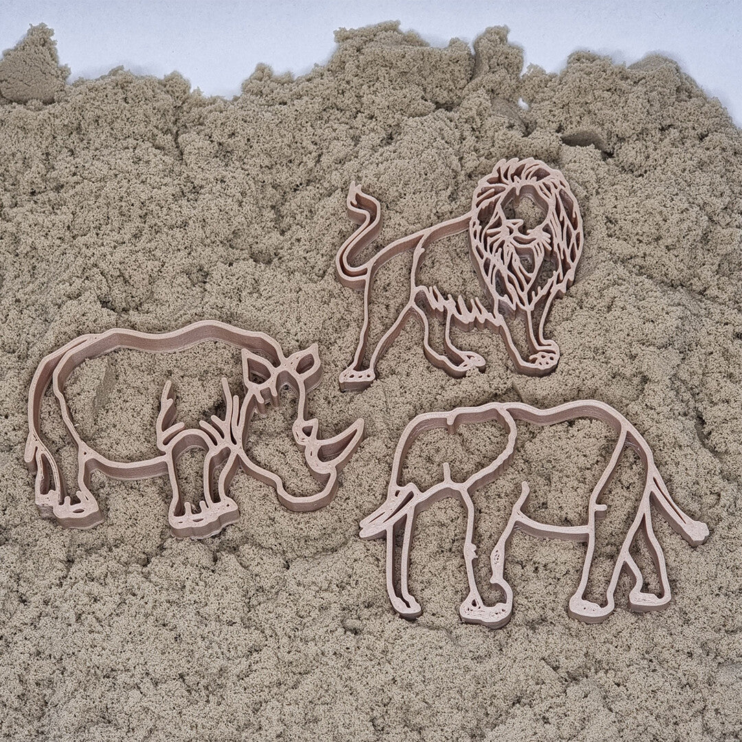 De drie beige uitsteekvormen van safaridieren, een neushoorn, leeuw en olifant, liggen in kinetisch zand.