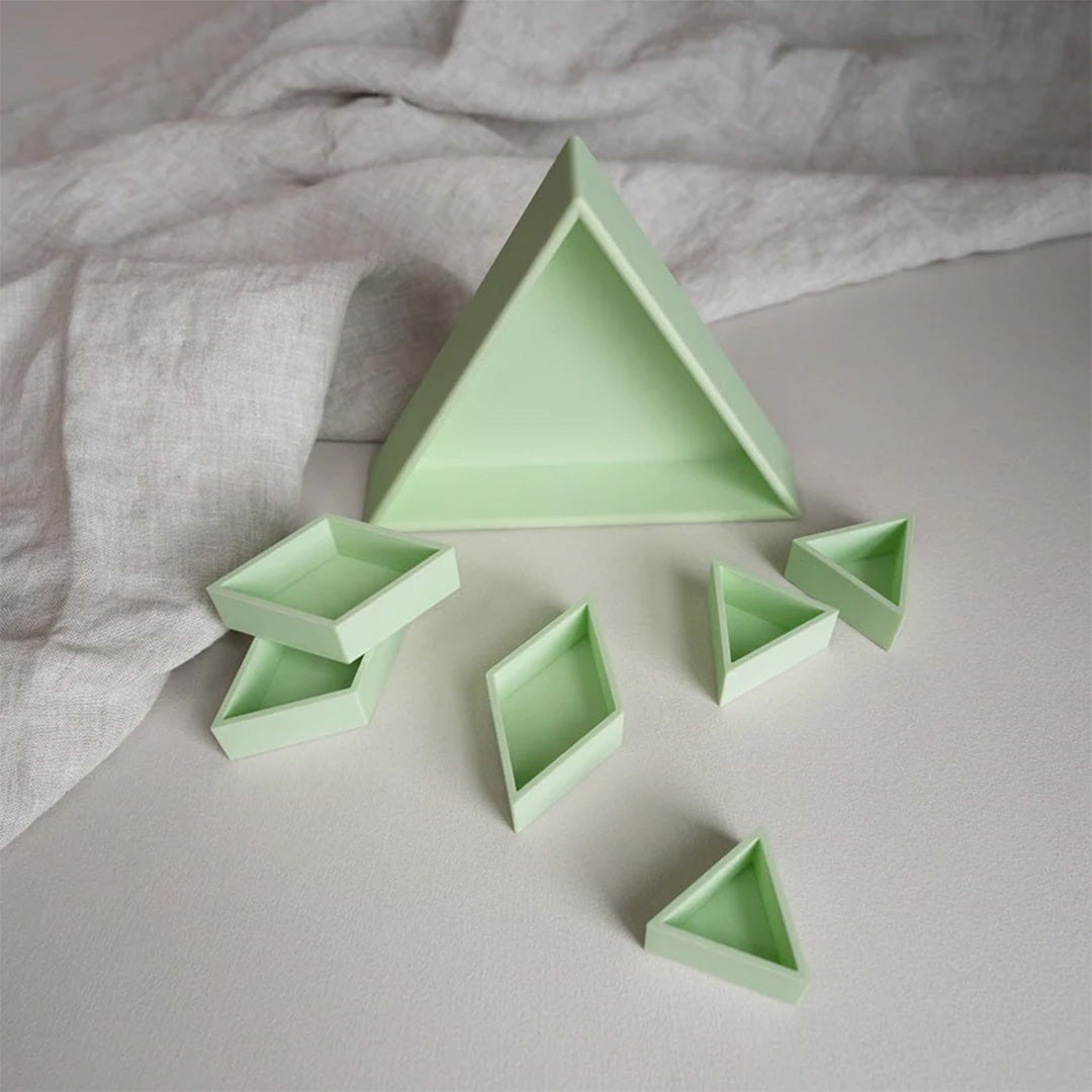 Grennn pastelgroene inlegdriehoek met diverse kleinere geometrische inlegbakjes, een sensorisch speelgoed, op een lichte ondergrond.