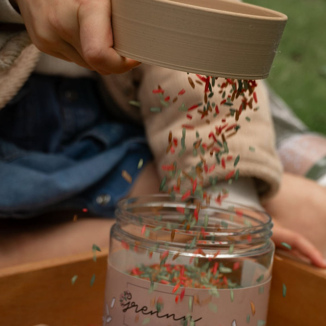 Kinderhanden zeven grennn speelrijst bosmix met een zeefje in een glazen pot.