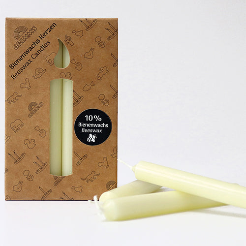 Drie grimm's crème bijenwaskaarsjes liggen voor de bruine verpakking.