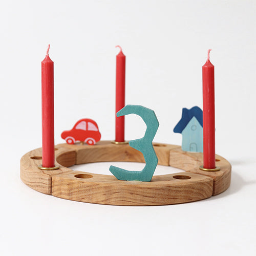 Drie rode Grimm's bijenwaskaarsen in een houten verjaardagsring met decoraties.