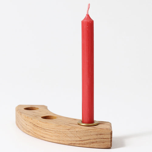 Een rode bijenwaskaars in een messing houder op een gebogen houten kaarsenstandaard.