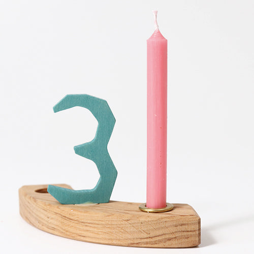 Roze verjaardagskaarsje in een houten houder met het blauwe cijfer 3.