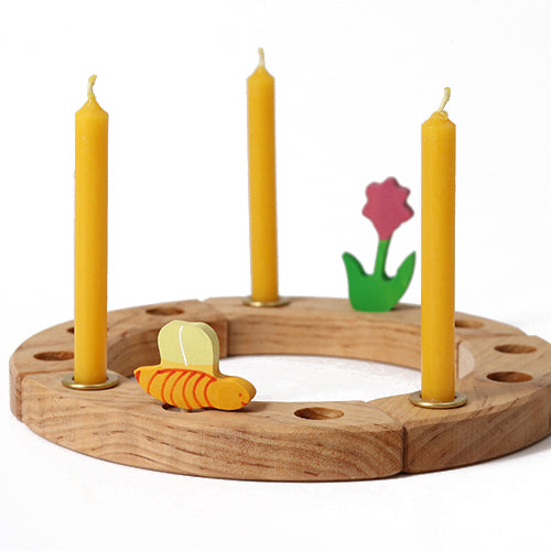 Drie gele bijenwaskaarsjes in een houten kaarsenring met houten decoraties van een bij en een bloem.