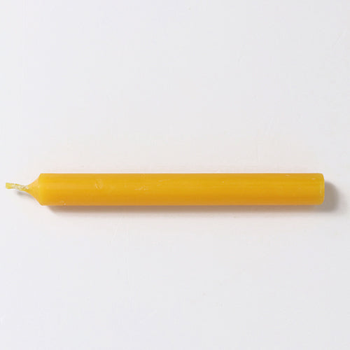 Eén geel bijenwaskaarsje ligt horizontaal op een witte ondergrond.