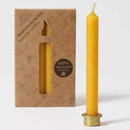 Een geel Grimm's bijenwaskaarsje staat in een gouden houder voor de kartonnen verpakking.
