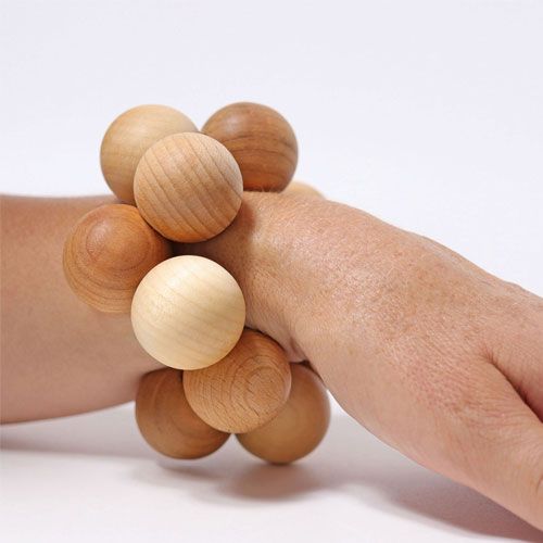 Een hand draagt het Grimm's houten babygrijpspeeltje van ballen als een armband.
