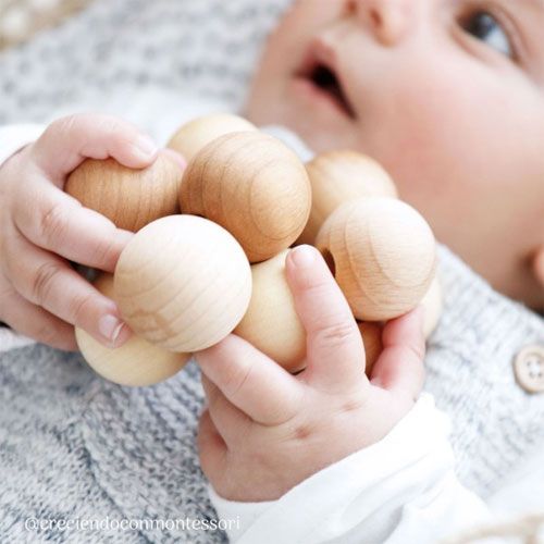 Een baby houdt het Grimm's houten babygrijpspeeltje van ballen vast met beide handjes.
