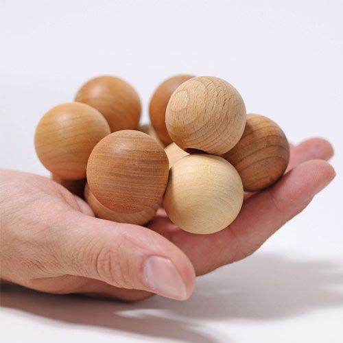 Een volwassen hand houdt het Grimm's houten babygrijpspeeltje van ballen vast om de grootte te tonen.