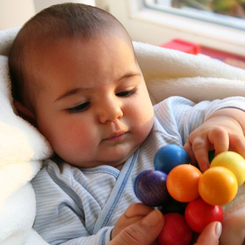 Een baby speelt met het Grimm's regenboog babygrijpspeeltje.