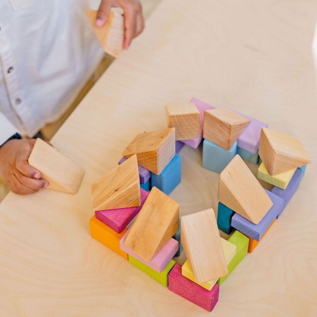 Kinderhanden spelen met grimm's houten bouwblokken op een houten tafel, waarbij een constructie van pastelkleurige en natuurlijke blokken wordt gebouwd.
