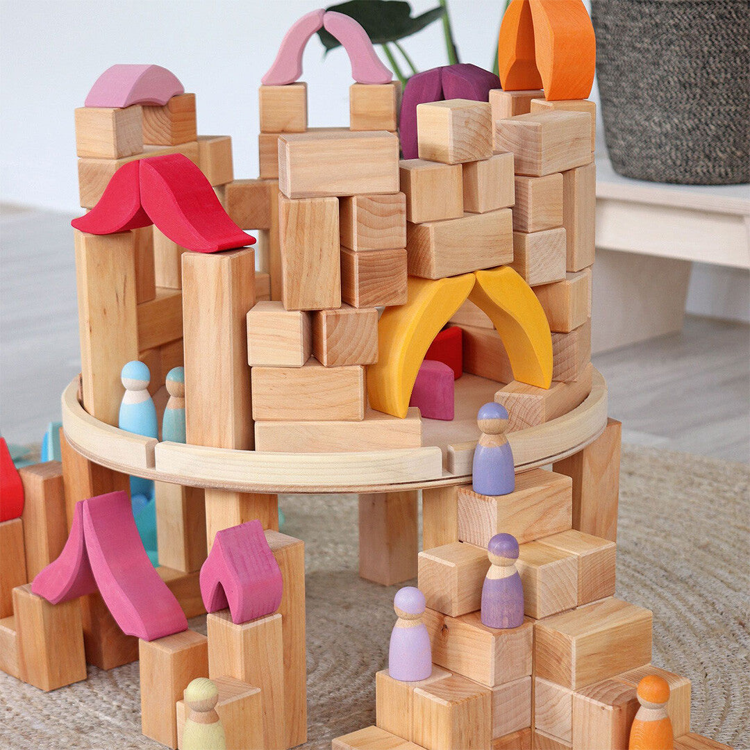 Een kasteelachtige constructie gebouwd van Grimm's houten bouwblokken met gekleurde bogen en houten poppetjes.
