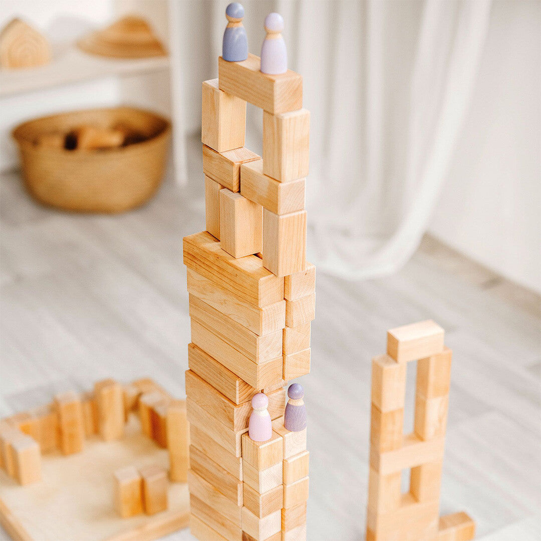 Een hoge toren gebouwd van Grimm's houten bouwblokken met houten poppetjes.