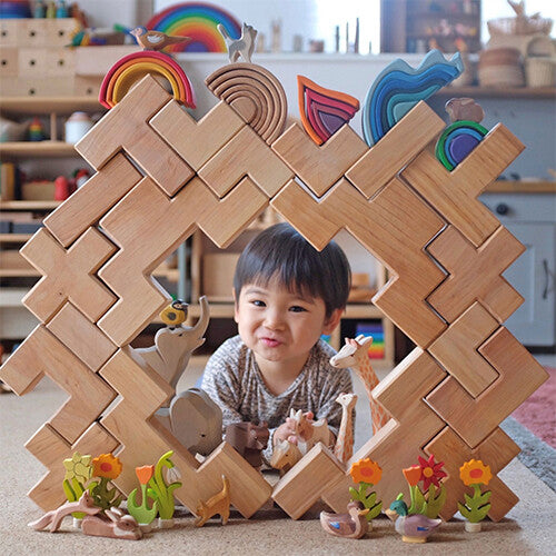 Een kind kijkt door een vierkant raam van Grimm's natuurlijke houten bouwblokken, versierd met houten dieren en planten.