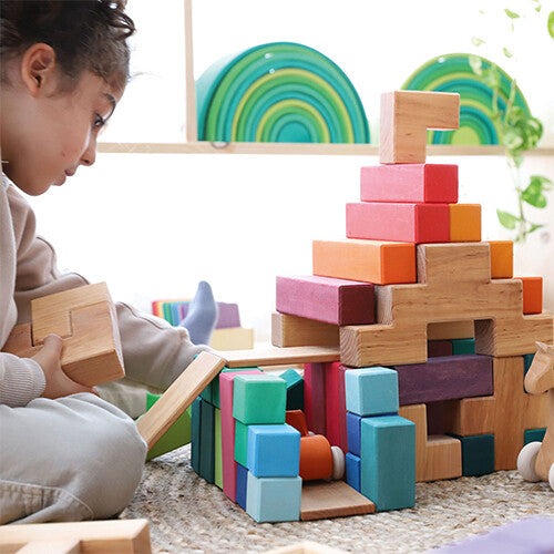 Een kind speelt met een grote constructie van Grimm's houten bouwblokken in natuurlijke en gekleurde tinten.