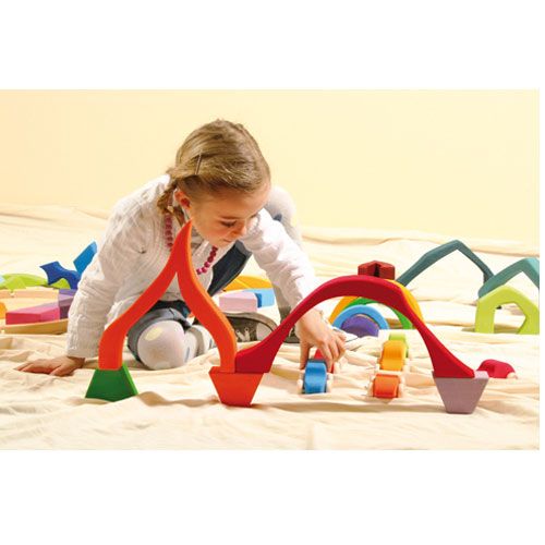 Een kind speelt met Grimm's houten bouwblokken en bouwt een brug met kleurrijke boogvormige blokken en kleine autootjes.