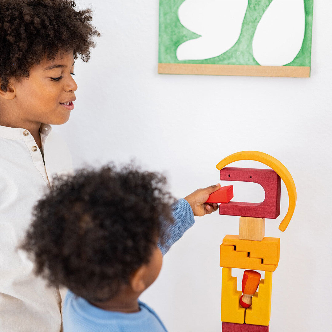 Twee kinderen spelen samen met Grimm's houten bouwblokken, opgebouwd als een toren.
