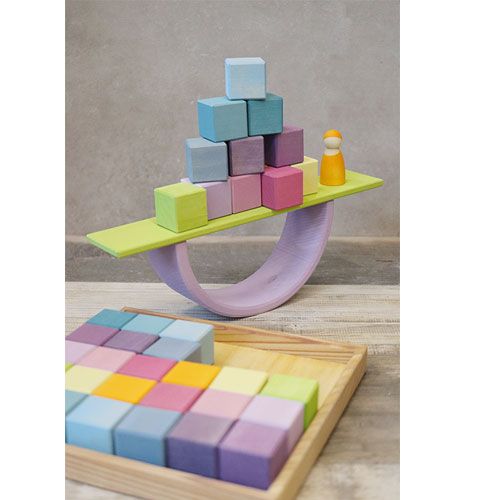 Houten balansspeelgoed met pastelkleurige blokken en een peg doll, met een bakje blokken op de voorgrond.