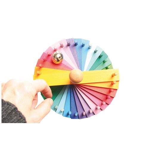 Een hand houdt een Grimm's regenboogkleurig houten onderdeel van de knikkerbaan met een gouden balletje vast.