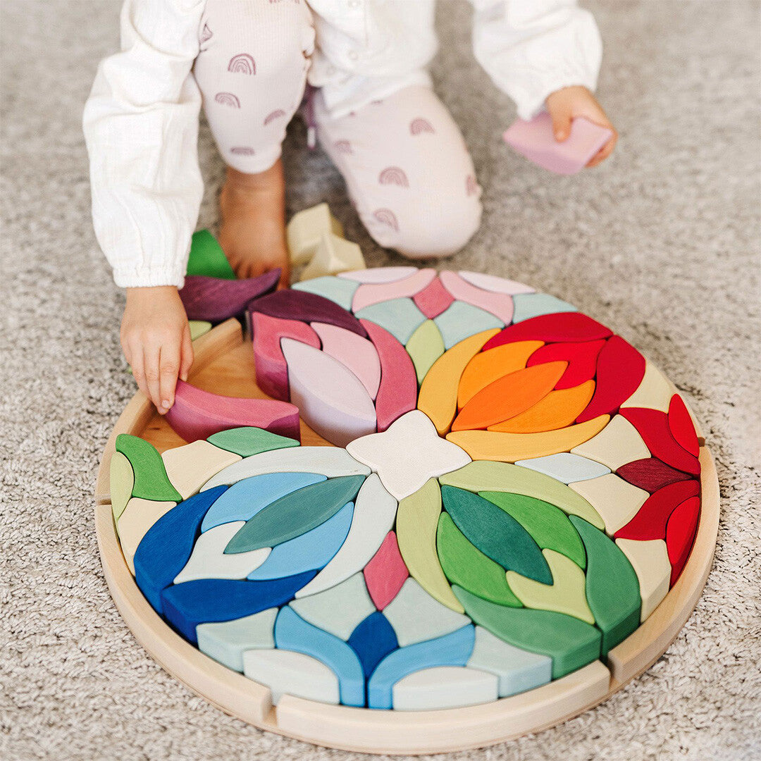 Een kind speelt op een grijze vloer met de grimm's houten puzzel 'Lara' met bloemvormige stukken.
