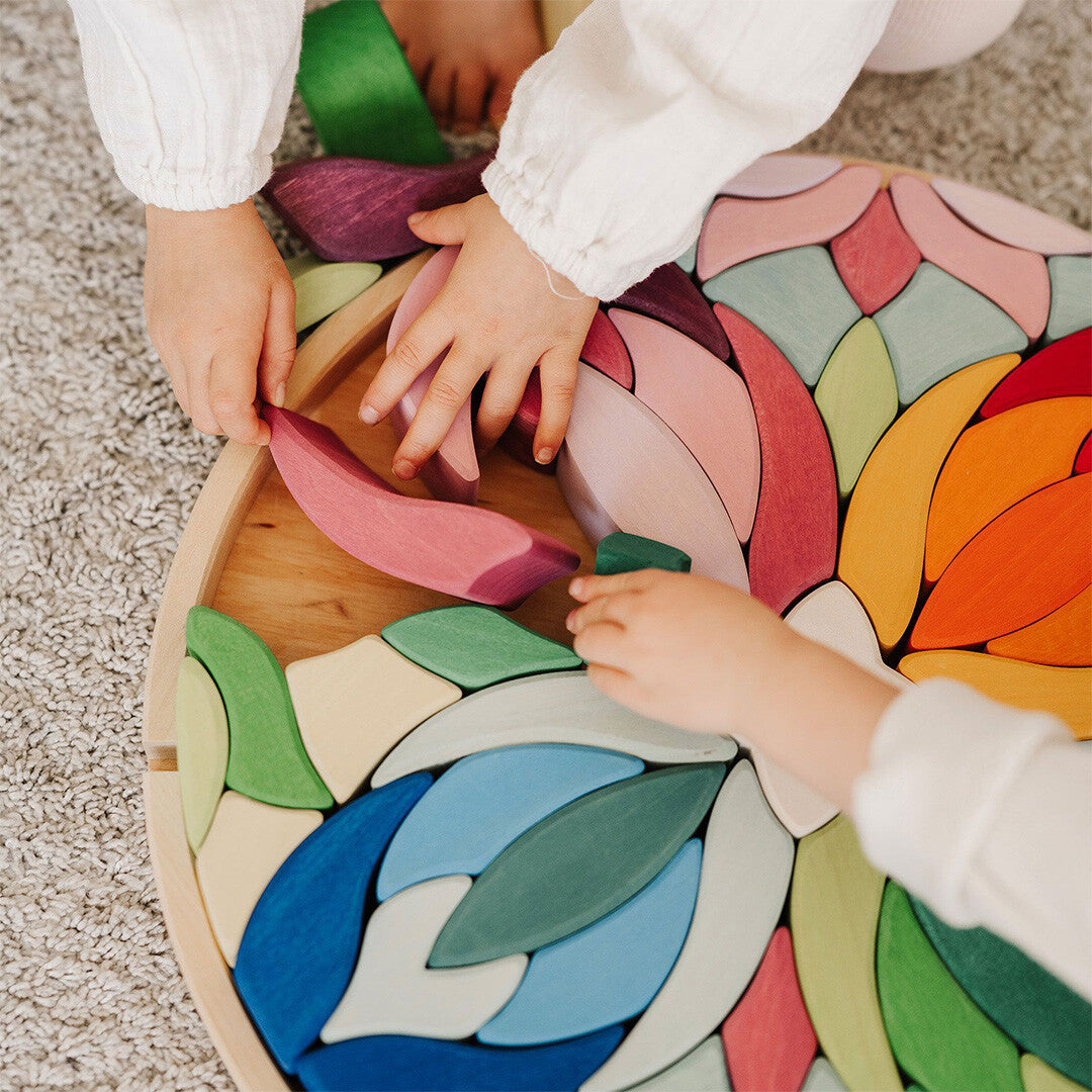 Twee kinderhanden plaatsen kleurrijke bloemvormige stukken in de grimm's houten puzzel 'Lara'.