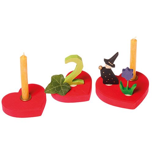 Grimm's houten decoratiefiguren met rode hartvormige kaarsenstandaards, waaronder een groen cijfer twee, een heks en een bloem.