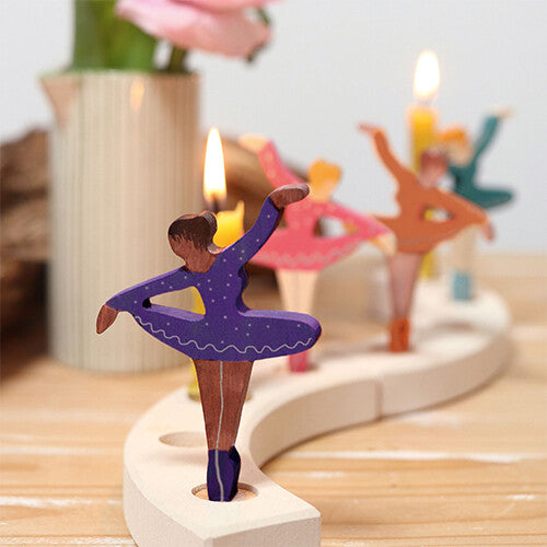De paarse Grimm's ballerina decoratie figuur staat in een houten kaarsenhouder met andere ballerina's en brandende kaarsen.