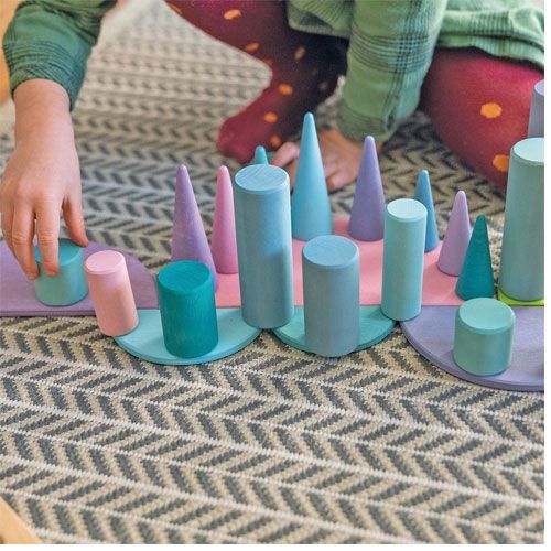 Een kind speelt met grimm's pastel houten bouwblokken en halfronde schijven op een vloerkleed.