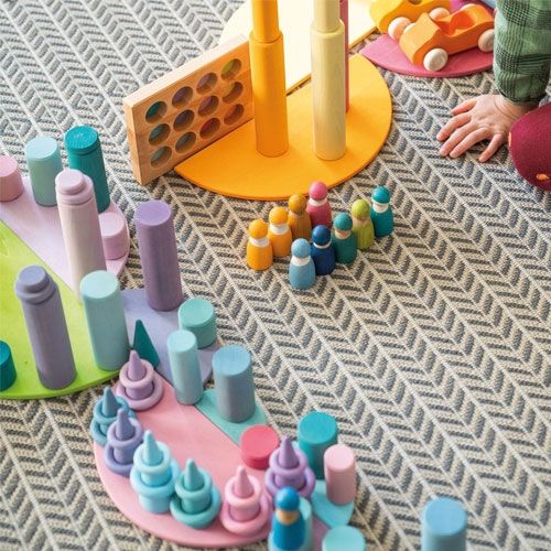 Een kind speelt met diverse grimm's pastel houten bouwblokken en figuren op een vloerkleed.
