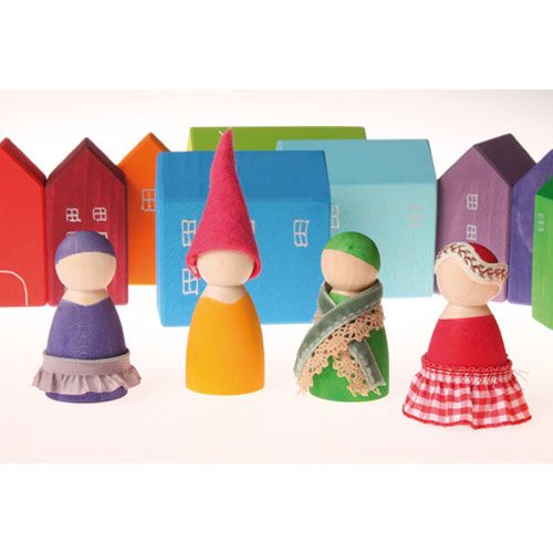 Vier grimm's houten poppetjes met stoffen kleding en mutsen, voor een rij gekleurde houten huisjes.