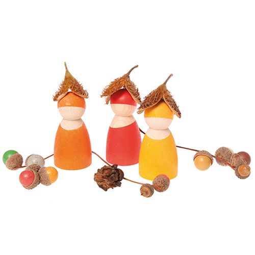 Drie houten poppetjes met herfstthema, versierd met eikeldopjes, omringd door eikels en takjes.