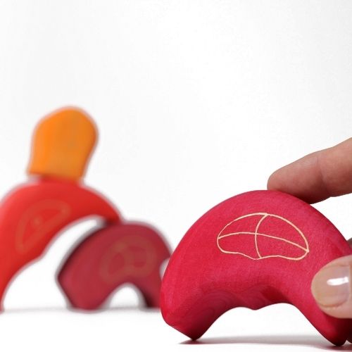 Een hand houdt een rood gebogen houten blok van het Grimm's kabouterhuisje vast.