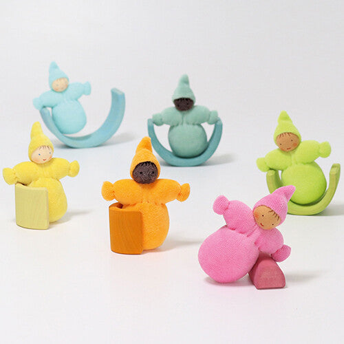 Zes grimm's kabouter poppen in pastelkleuren zitten op of leunen tegen verschillende houten blokken en vormen.