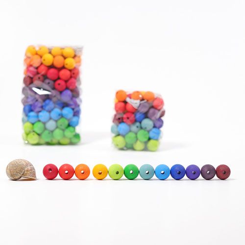 Grimm's houten regenboogkralen in een rij naast een slakkenhuis, met verpakkingen op de achtergrond.