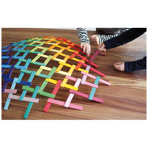 Twee kinderen weven Grimm's houten regenboog latten bouwspeelgoed tot een kleurrijk patroon op de vloer.
