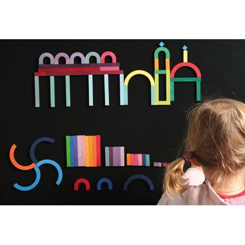 Een kind kijkt naar een zwarte magneetplaat met daarop kleurrijke Grimm's houten magneetpuzzelstukken die een kasteel en andere vormen creëren.