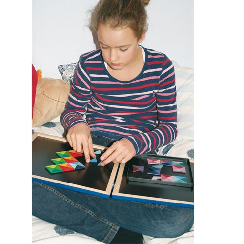 Een kind speelt met de Grimm's houten magneetpuzzel, waarbij ze kleurrijke driehoekige stukken op een open zwarte speelplaat legt.