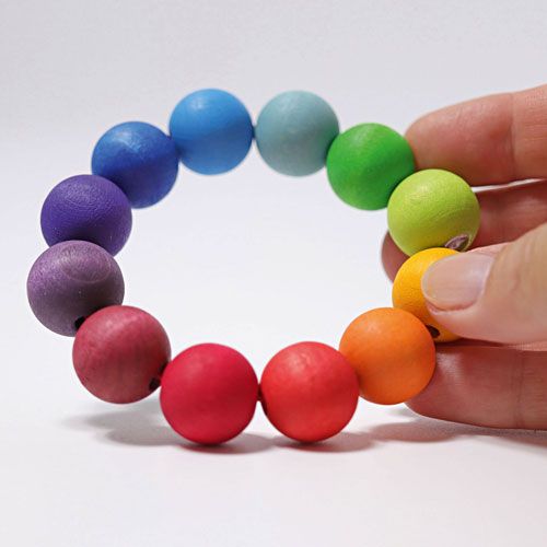 Een hand houdt de Grimm's houten regenboog parelring vast, wat de grootte van het babyspeelgoed toont.