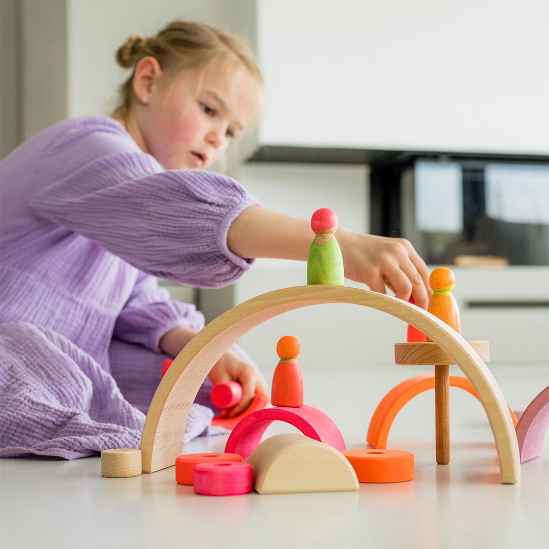 Een meisje speelt met Grimm's houten popjes en gekleurde houten bogen en ringen.