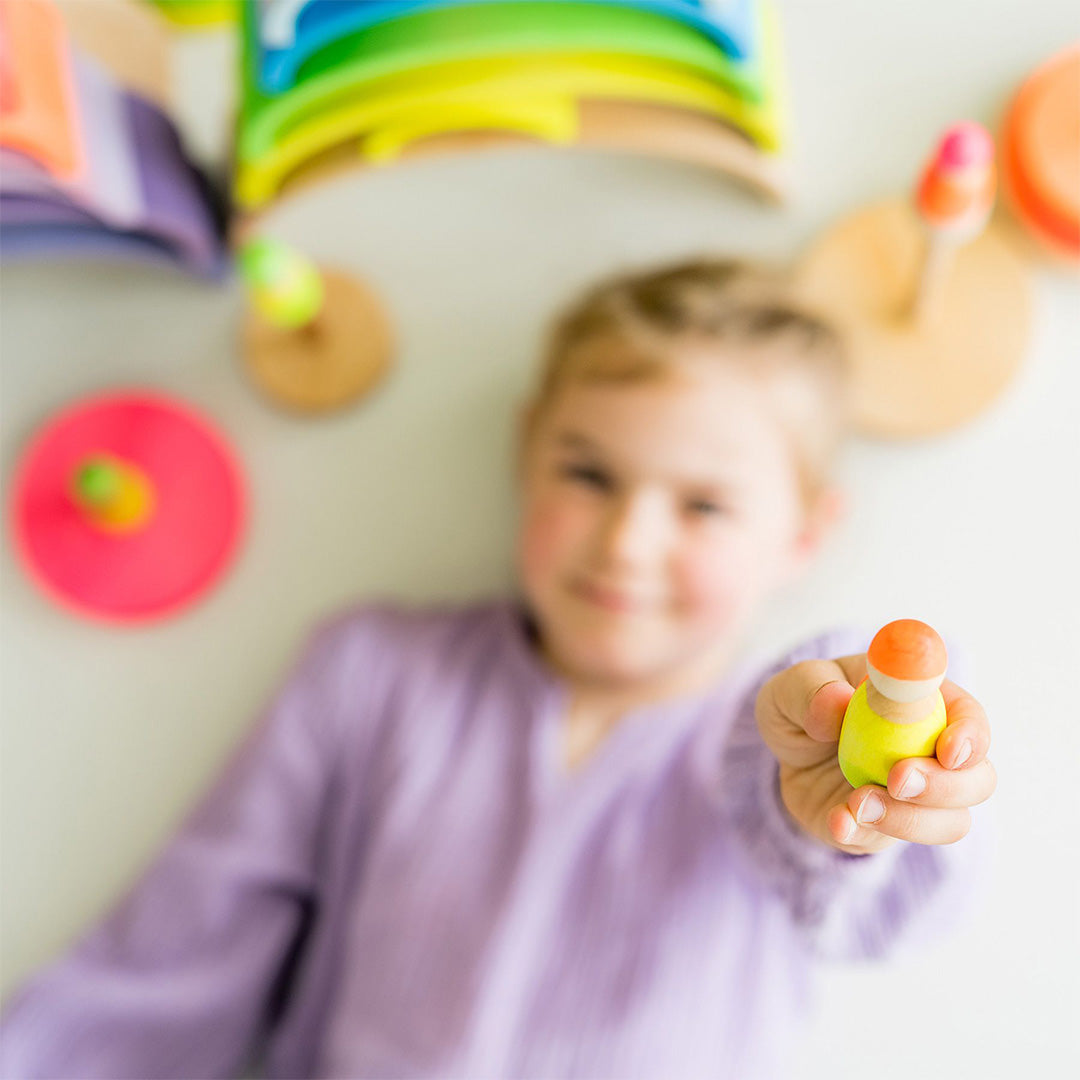 Een kinderhand houdt een Grimm's houten popje in geel en oranje vast.