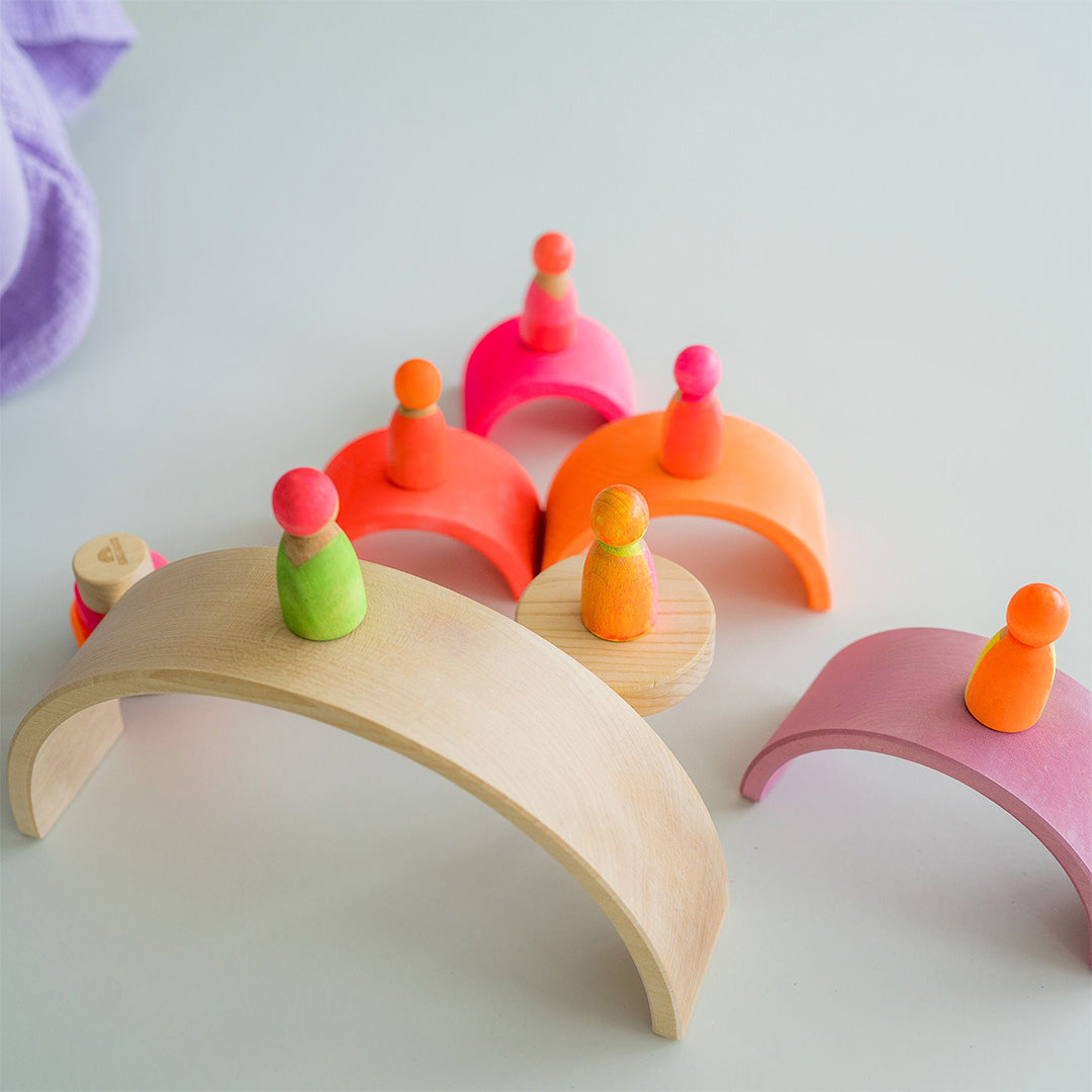Grimm's neon roze houten popjes staan op en rondom houten regenboogbogen.