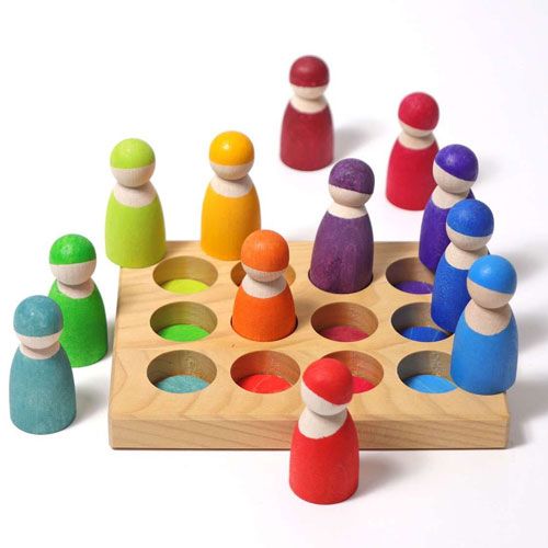 Twaalf grimm's houten peg dolls in regenboogkleuren in en rondom een houten sorteerbak met gekleurde vakken.