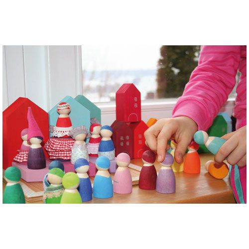 Een kind speelt met grimm's houten peg dolls en huisjes in regenboogkleuren op een tafel.