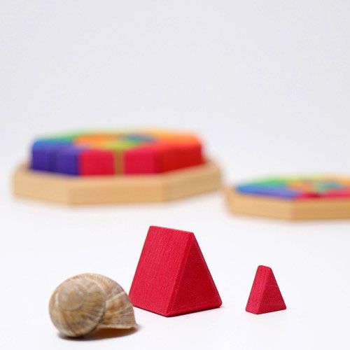 Een slakkenhuis naast twee rode houten driehoekige puzzelstukjes van verschillende grootte.