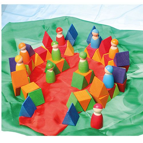 Een speelscène met grimm's veelkleurige houten puzzelstukken en houten poppetjes op rode en groene doeken.