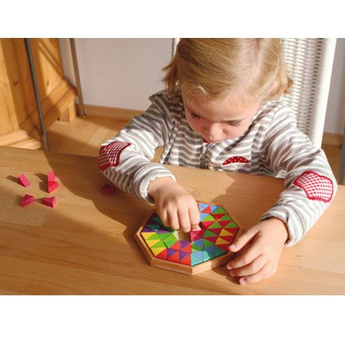 Een kind speelt aan een houten tafel met de Grimm's achthoekige houten puzzel, waarbij het veelkleurige driehoekige stukjes plaatst.