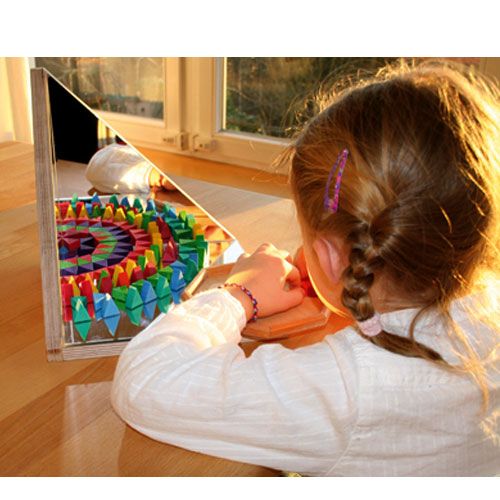 Een kind speelt met de Grimm's houten puzzel voor een spiegel, waardoor een caleidoscopisch effect ontstaat.